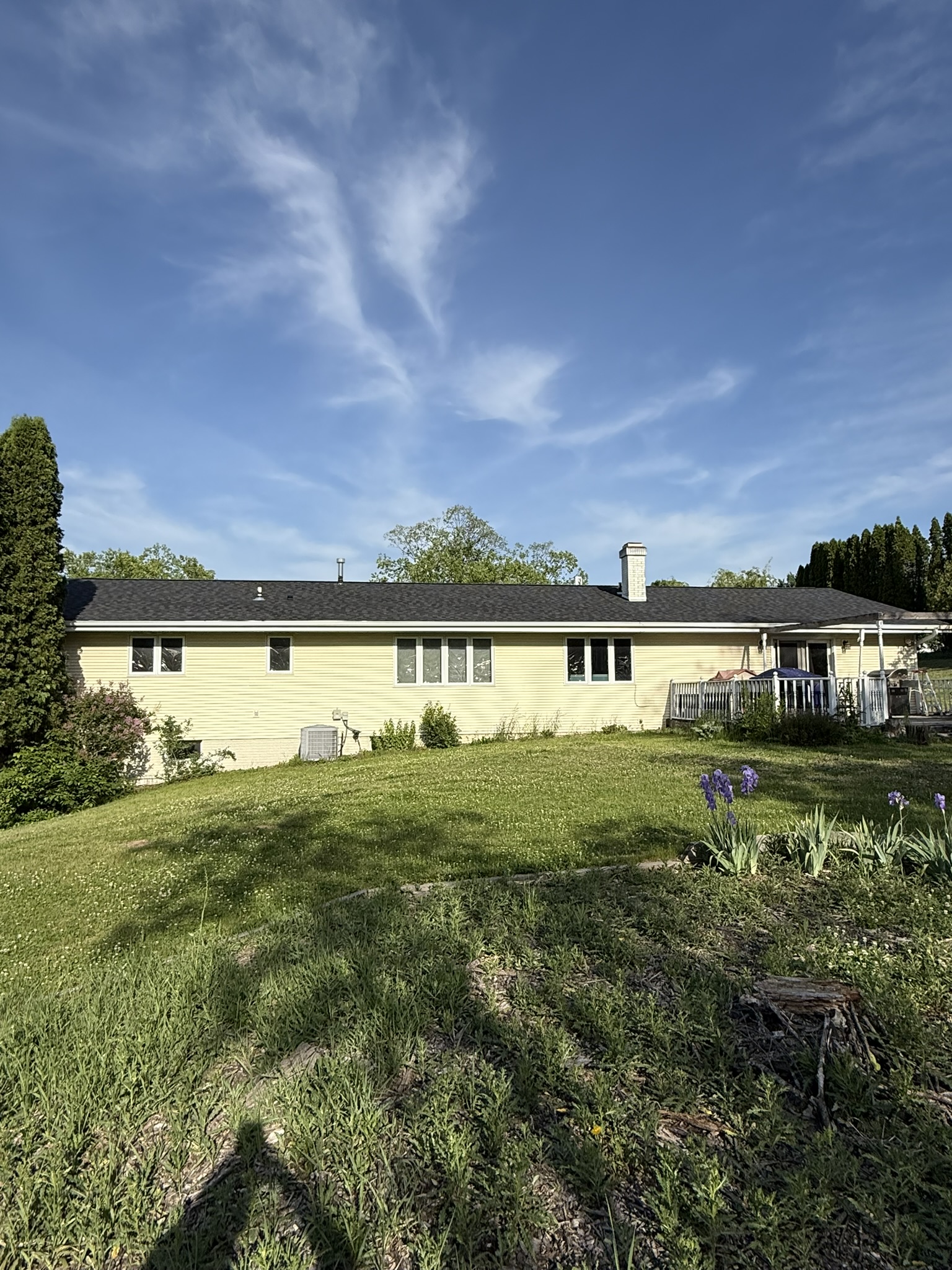 Rear of an established single-story ranch home with a back deck and mature trees